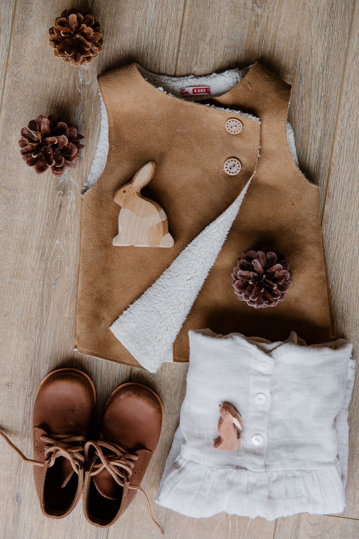 A tan vest, linen top and leather boots laid out on a timber floor.