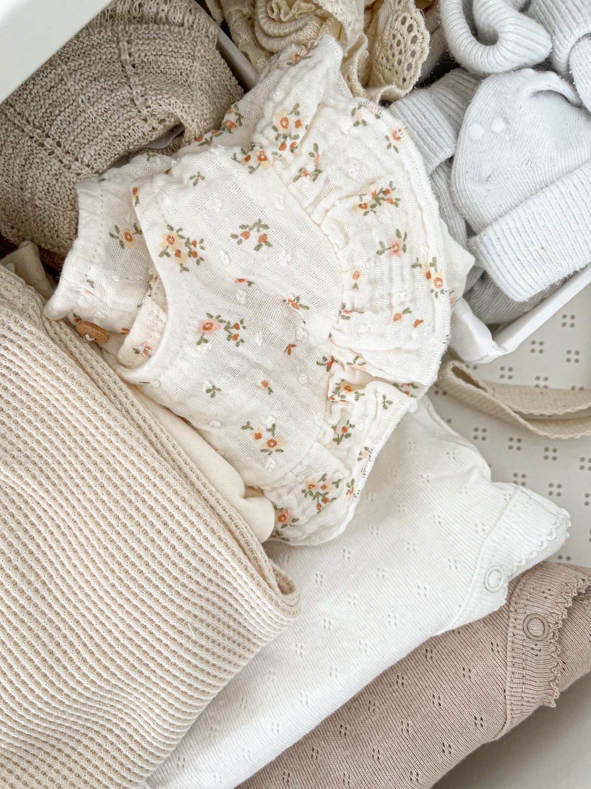 Folded baby knits and a pointelle bodysuit in cream and oatmeal.