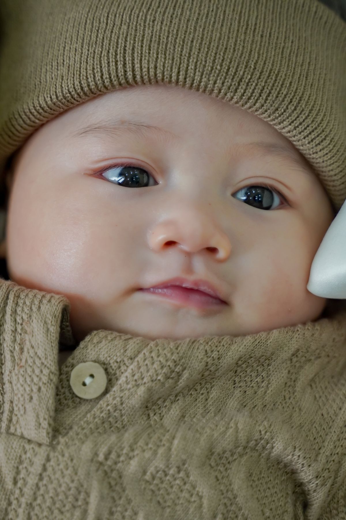 A baby in a sage knitted bonnet and textured romper with a shell button.