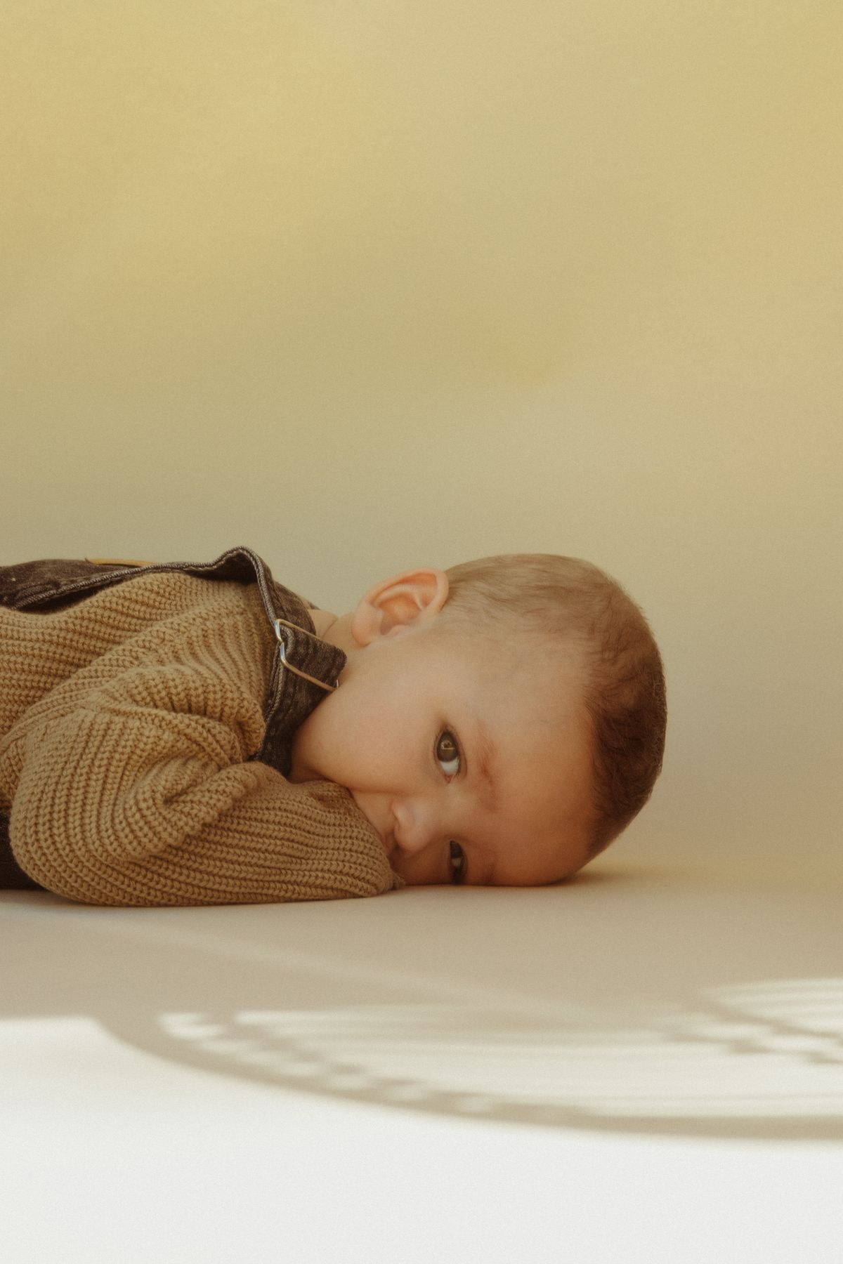 A baby in a knitted jumper resting on a warm sand backdrop in morning light.