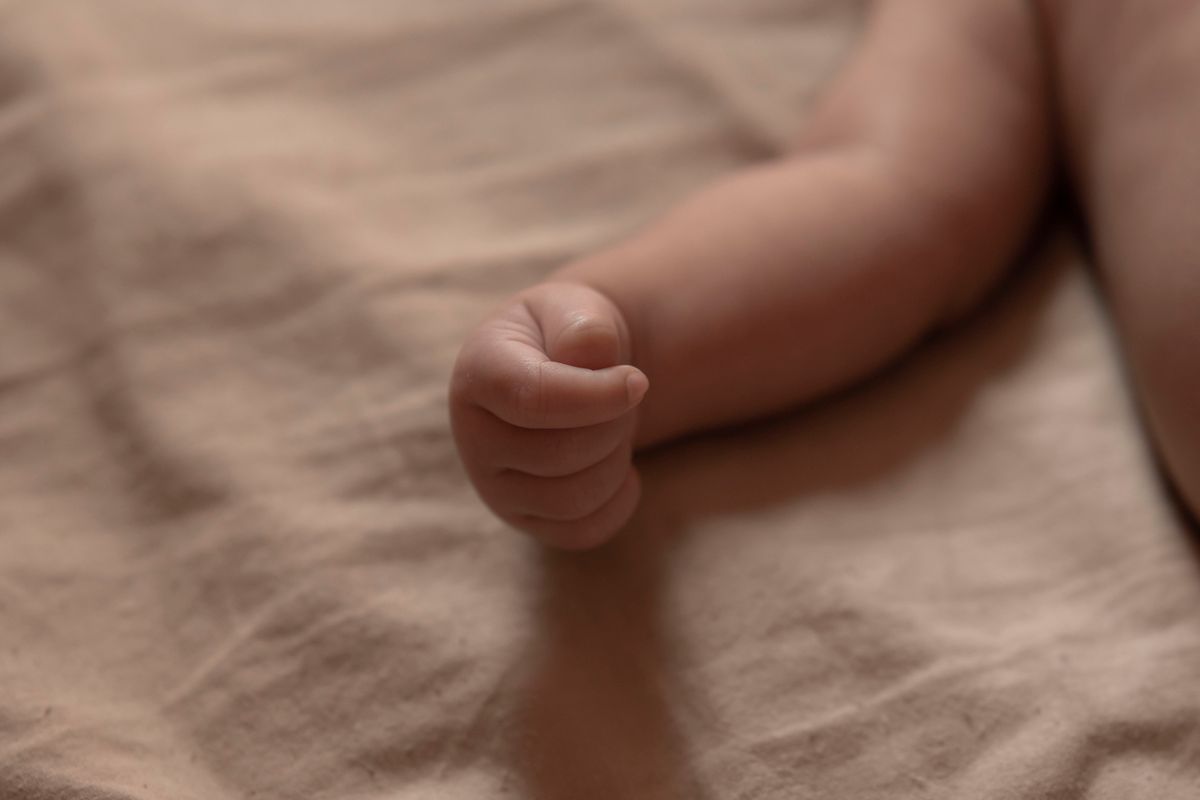 A newborn's hand curled on soft clay-coloured linen.