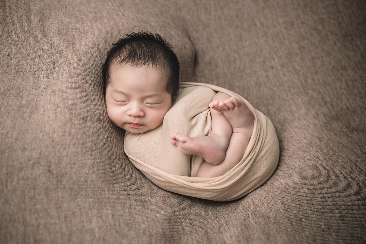 A sleeping newborn wrapped in a soft oatmeal blanket.